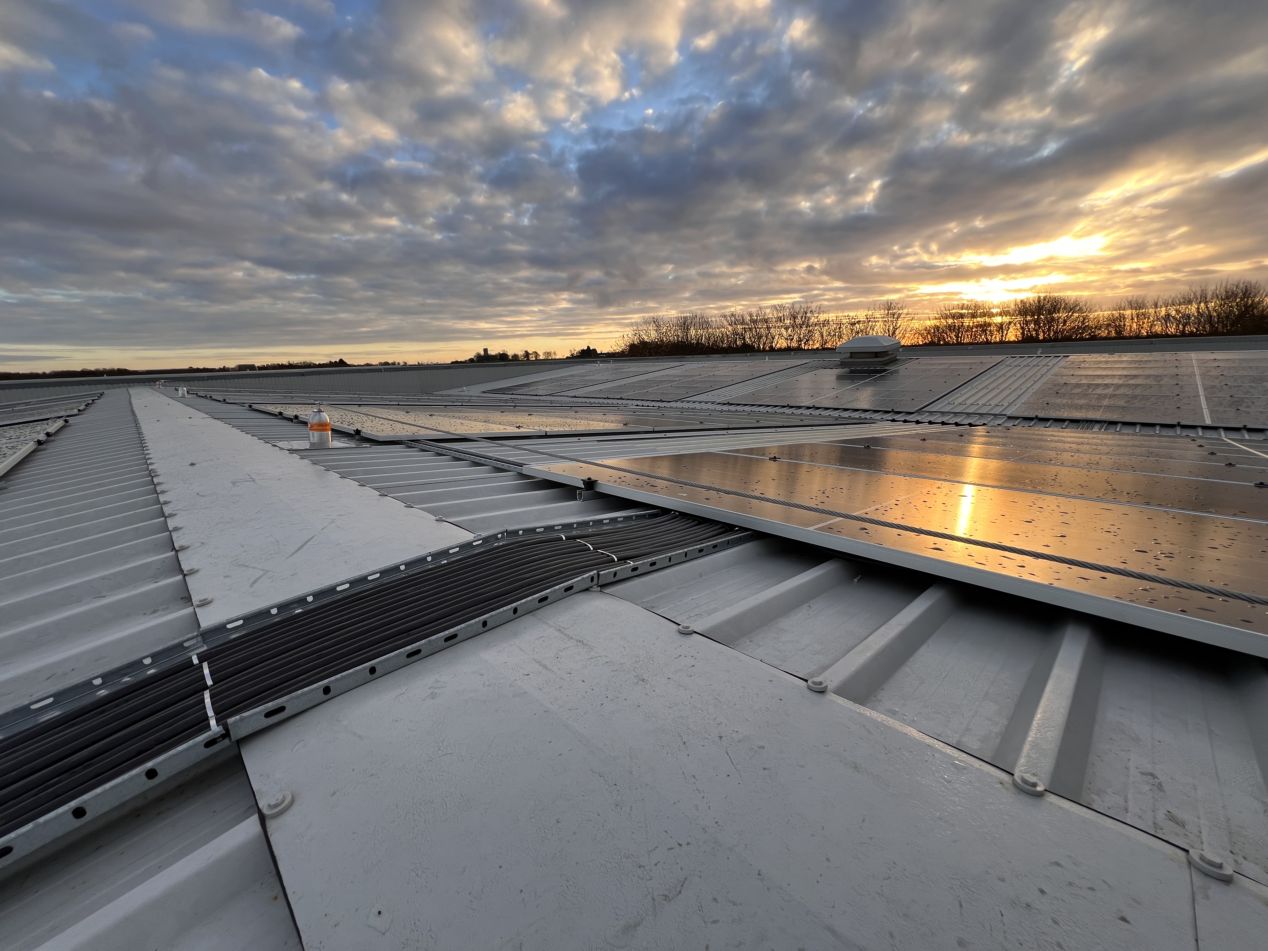 Rows of solar panels and cable trays on a profiled metal industrial roof at Paull at sunset